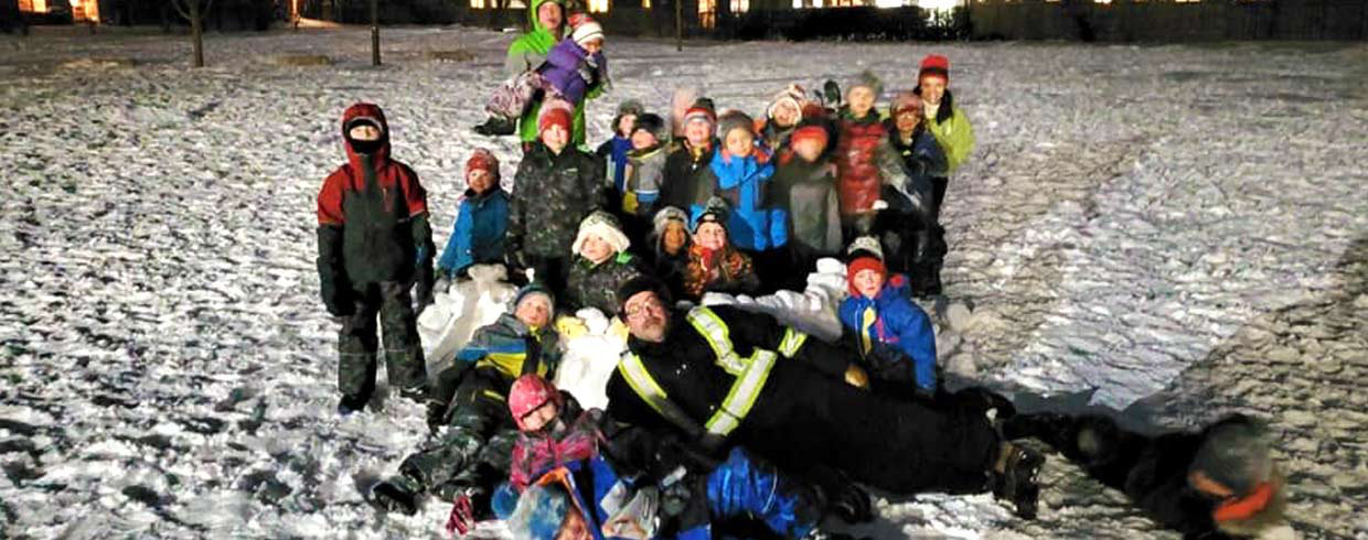 A group of young Scouts dressed for winter, posing outdoors while making a snow fort in the evening.