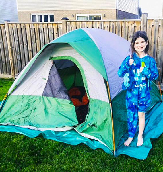 Young girl standing proudly beside her pop-up tent in her backyard.