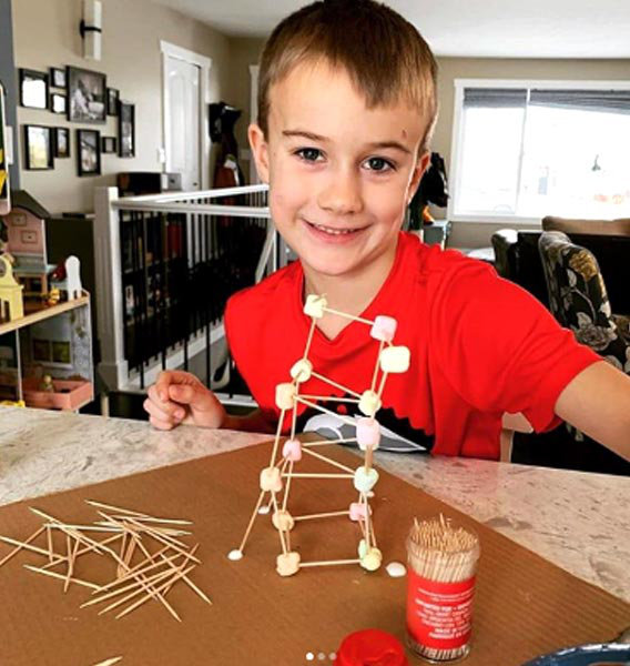 Cub scout proudly displaying a tower he built from toothpicks and marshmallows.