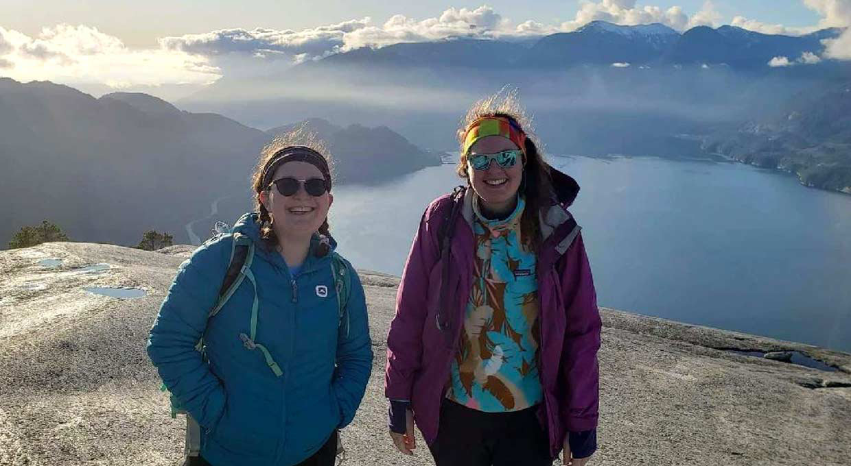 Two young women Rovers standing high atop a lookout point surrounded by mountains and water.