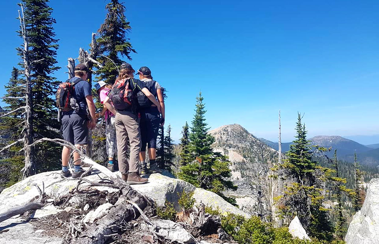 Four Scouts wearing backpacks are enjoying the view from a mountaintop vantage point.