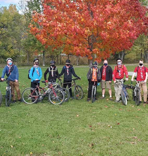 Group of 1st Uxbridge Scouts wearing masks and standing beside their bikes.