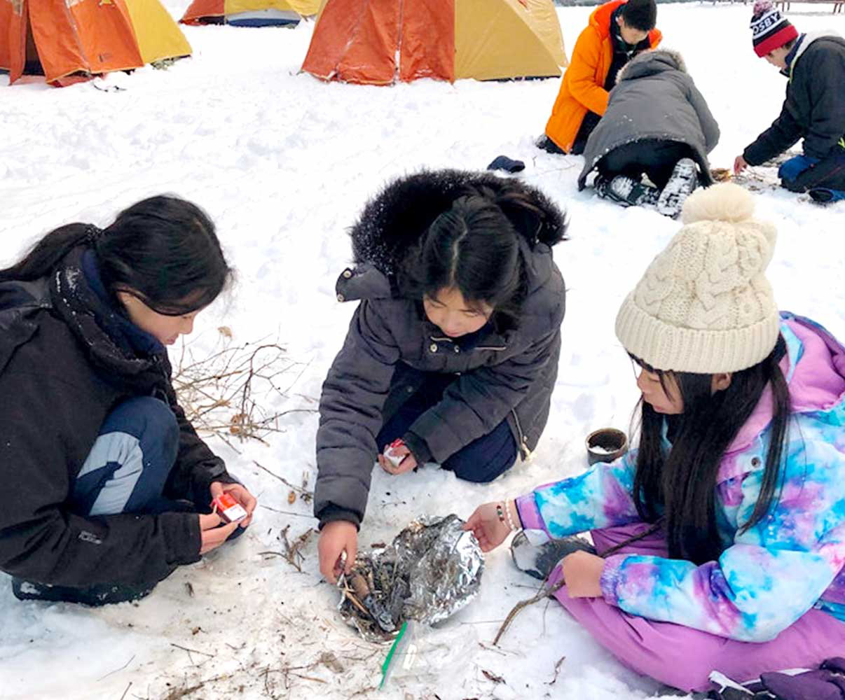 Three young girl Scouts making fire in the snow.