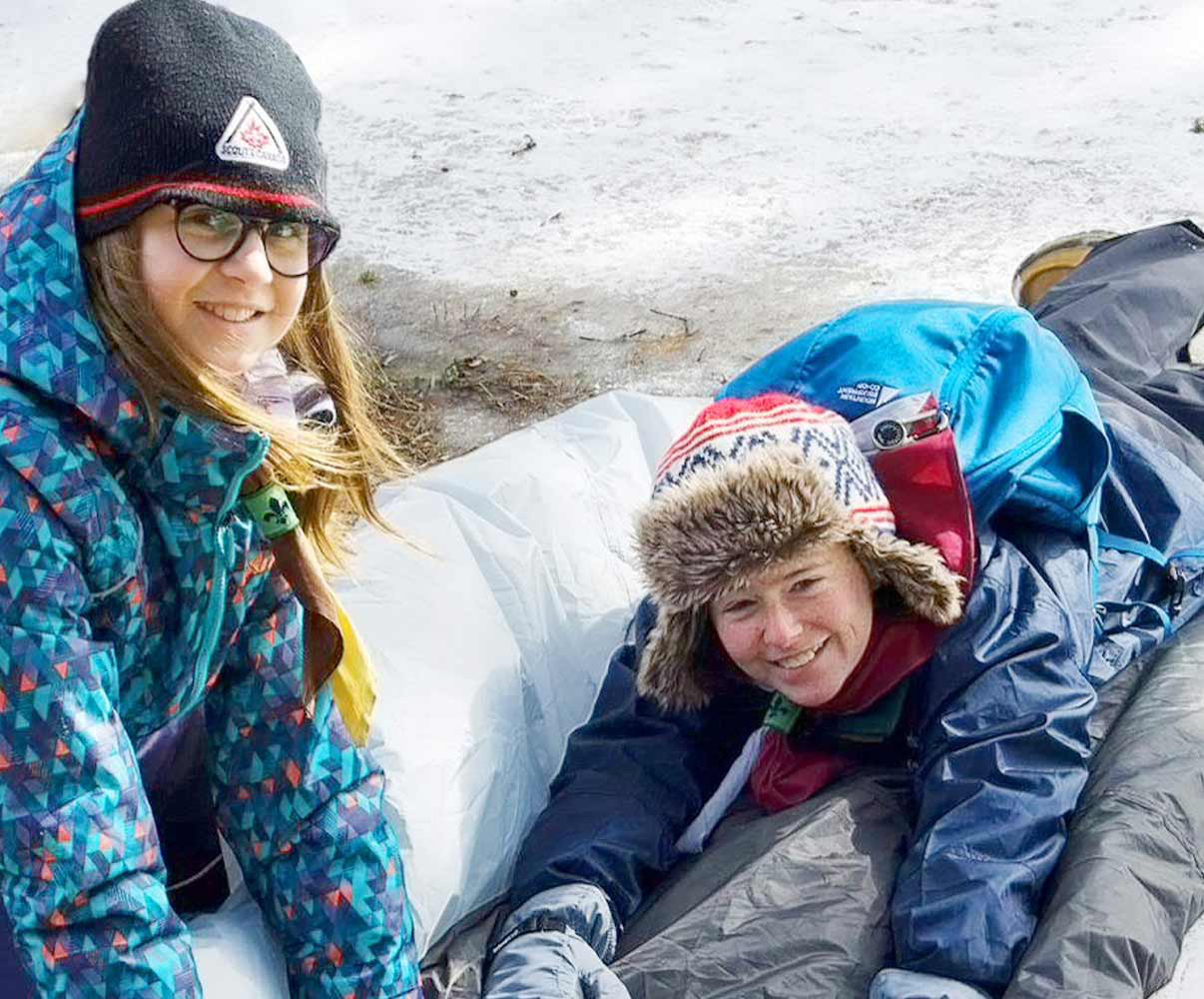 Two young girl Scouts prepare their sleeping bags for winter camping.