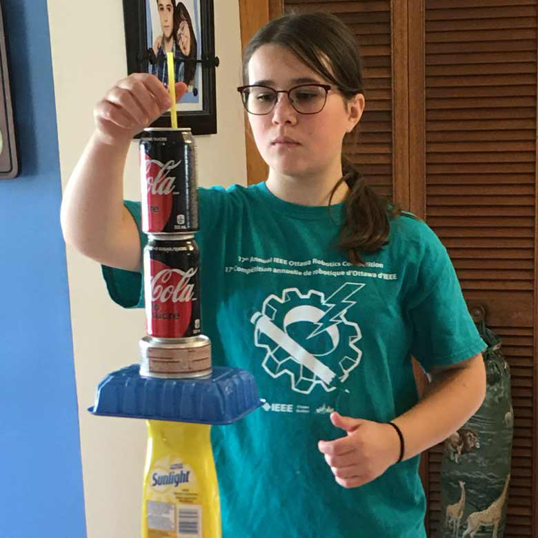 A girl Scout building a tall tower from bottles, cans and jars at home.