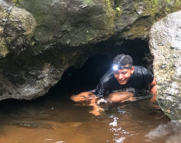 A Scout in the water with headlamp on searching inside a cave.