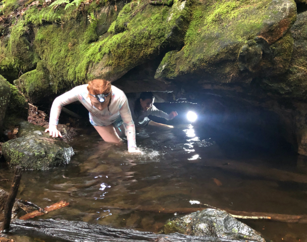 Two girl Scouts wearing head lamps in the water coming out of a cave.