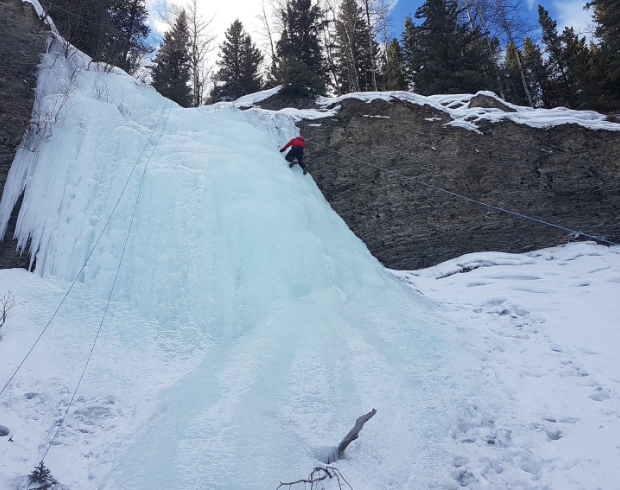 A view from below looking up to an ice climber with safety harness on climbing a steep ice cliff.